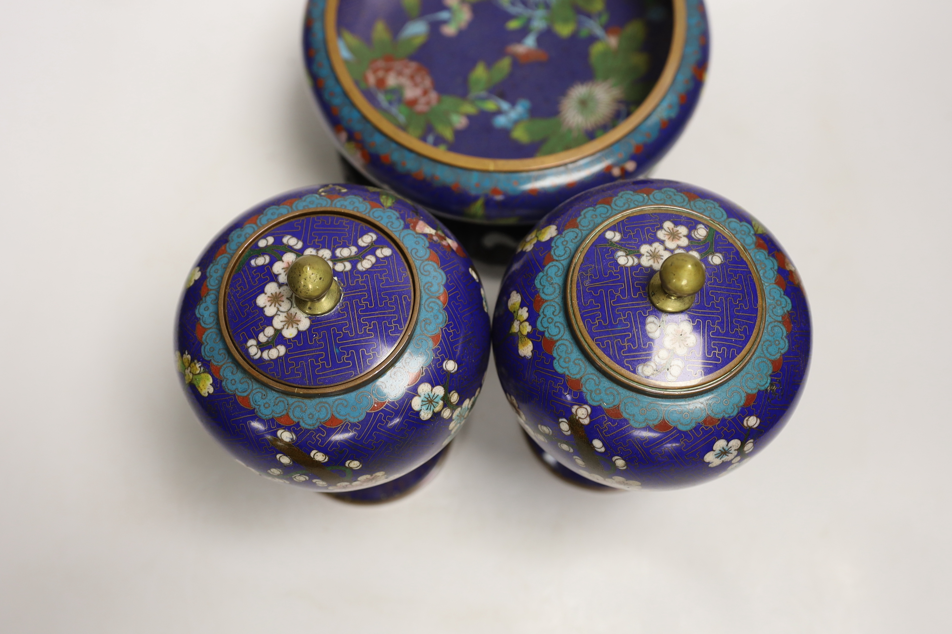 A pair of early 20th century Chinese cloisonné enamel jars and covers, together with a similar bowl and wood stand, largest 20cm high